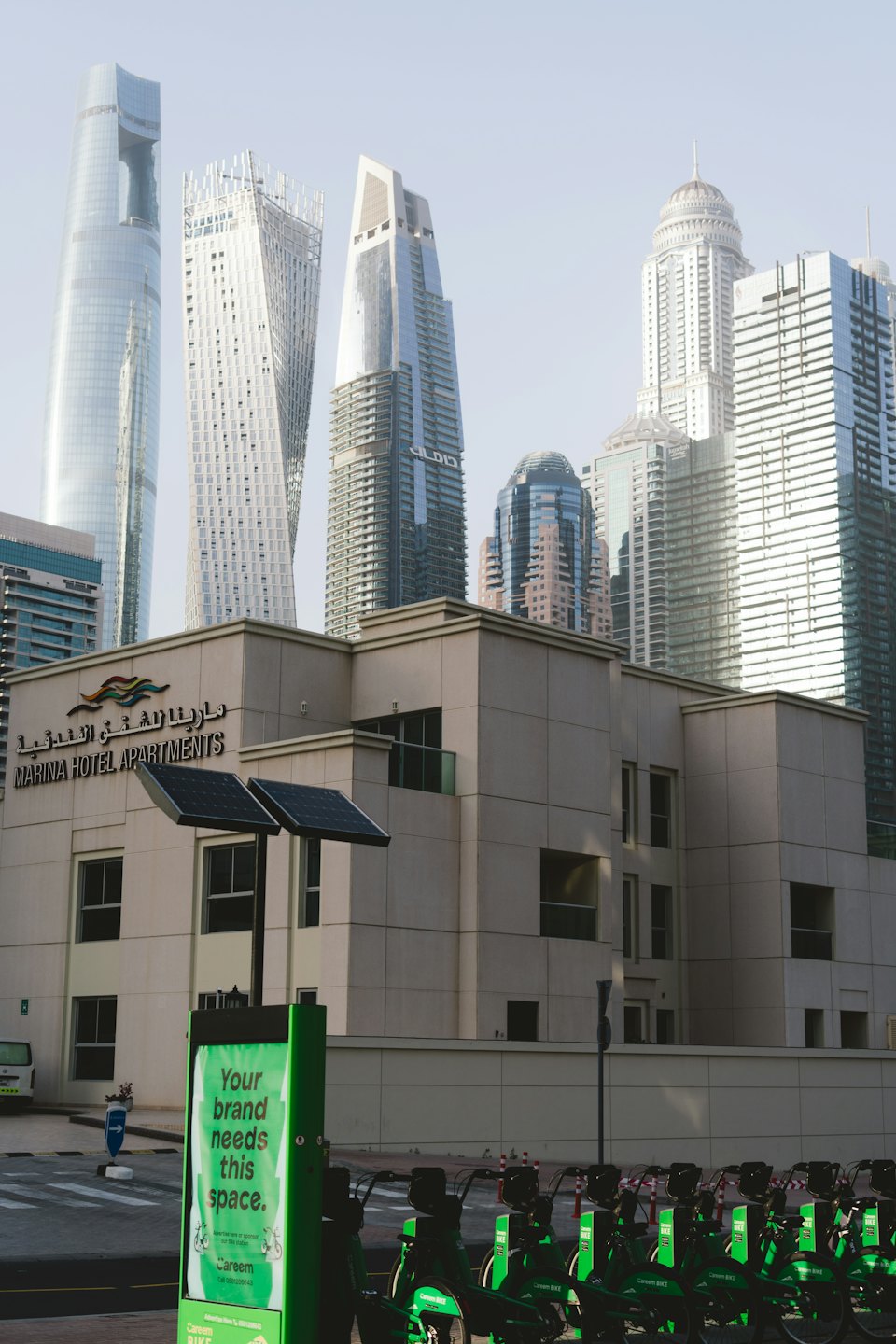 Sandfarbenes Marina Hotel Apartments Gebäude mit Solaranlagen in der Nähe einer Fahrradstation.