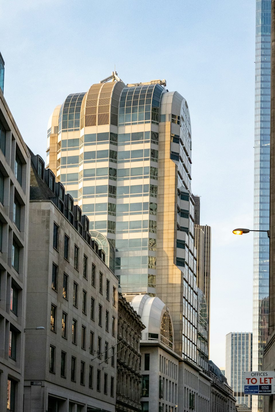Moderner Bürohochhaus mit geschwungener Dachkonstruktion neben älteren Gebäuden.